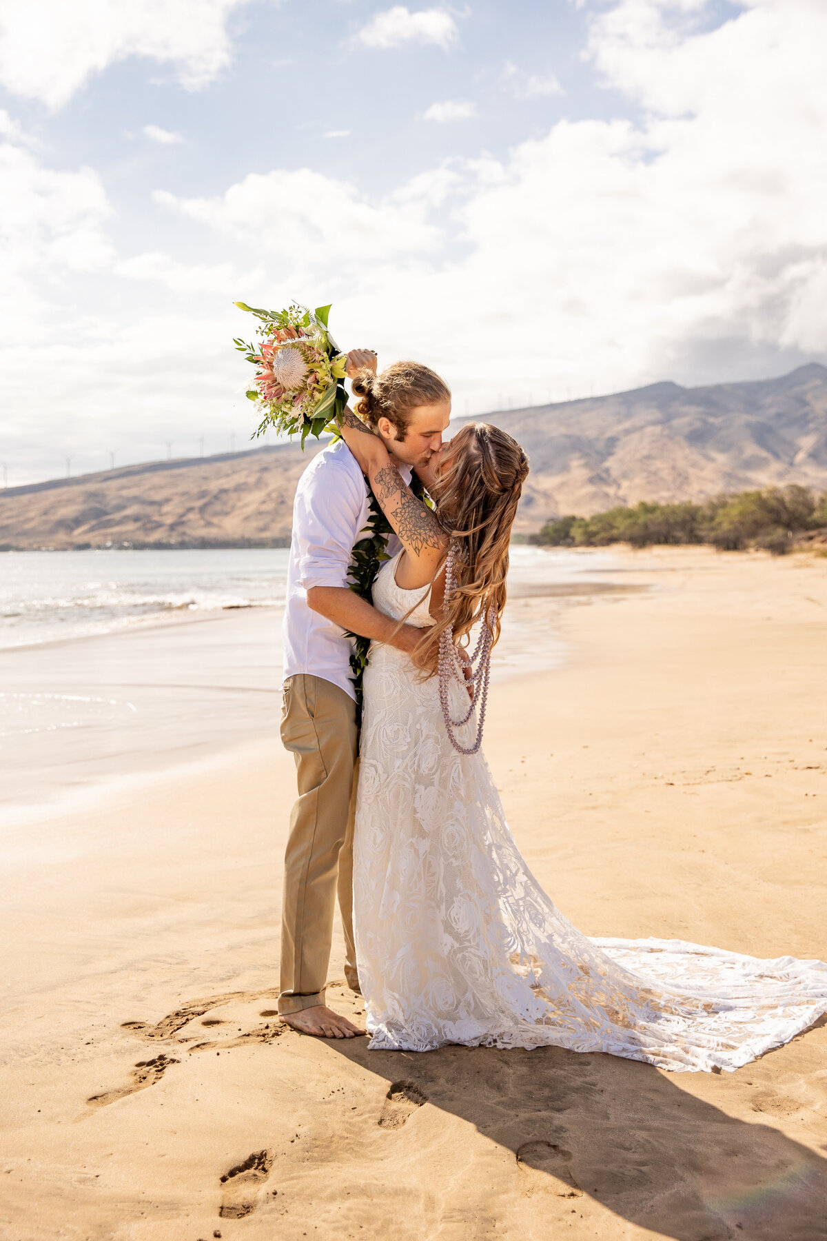 Maui Wedding Photographer captures bride and groom kissing on beach holding bouquet