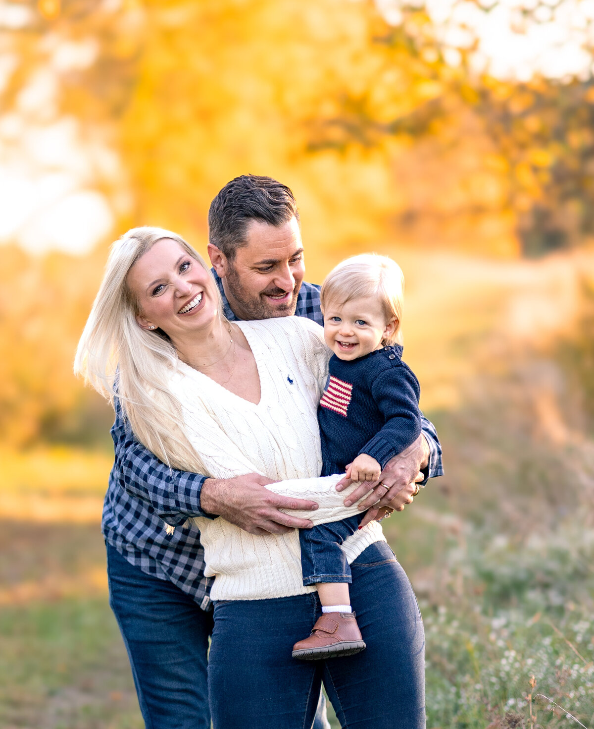 Dad wrapping arms around mom and baby at a park in Milford Michigan