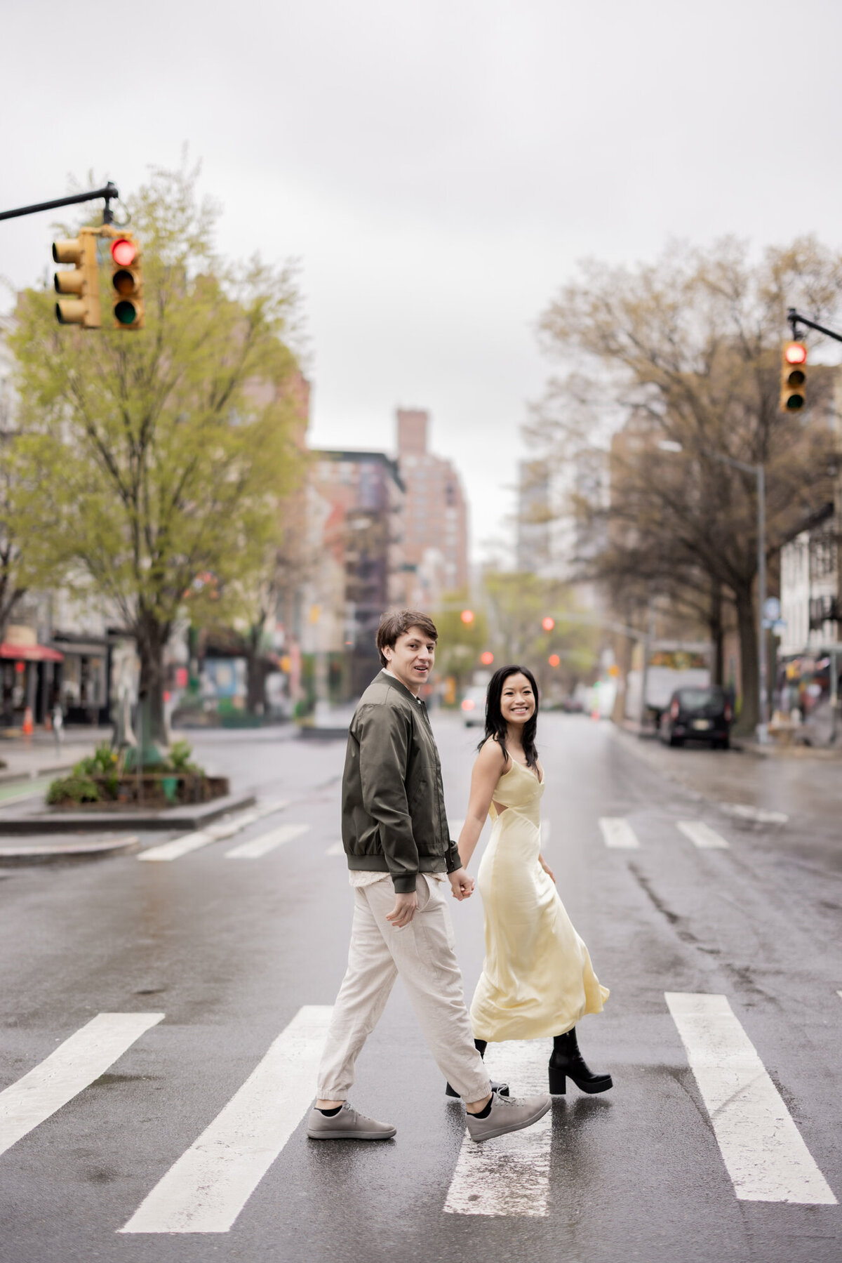 Smiling couple holding hands while walking through a crosswalk in New York City's West Village during a spring engagement session by Michelle Jackson Studio.