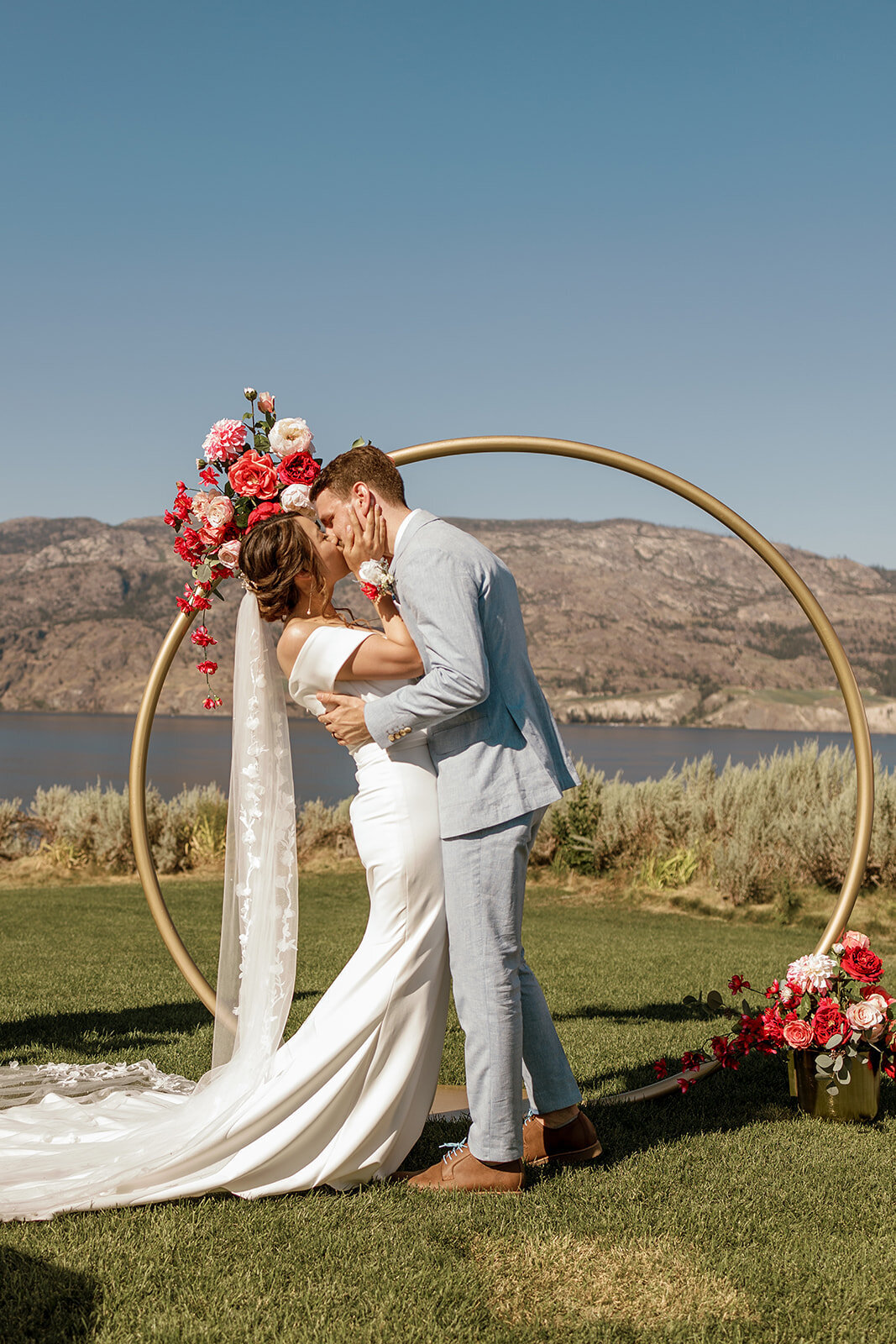 Wedding couple kiss each other in front of a modern gold arch adorned with monochromatic pink flowers.