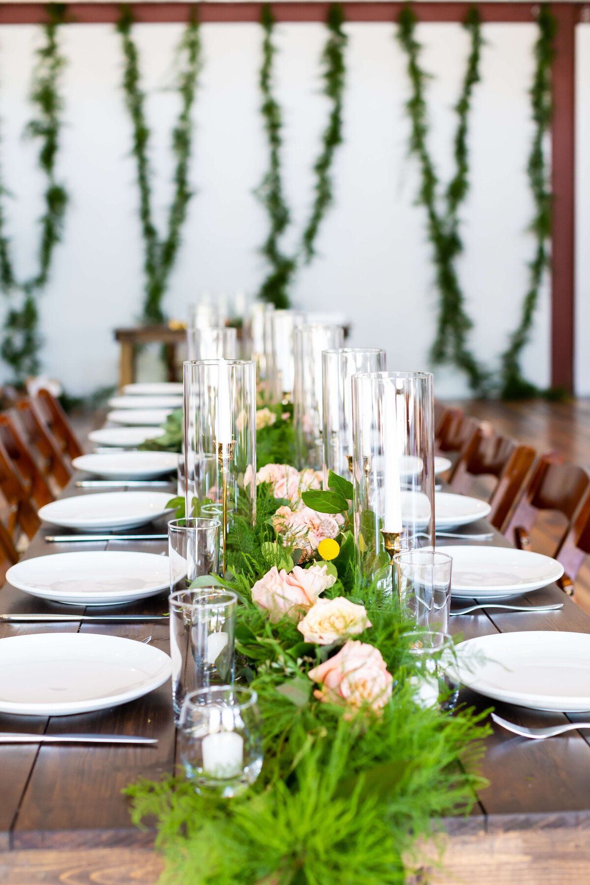 Wedding reception tables decorated with tall pillar candles and greenery