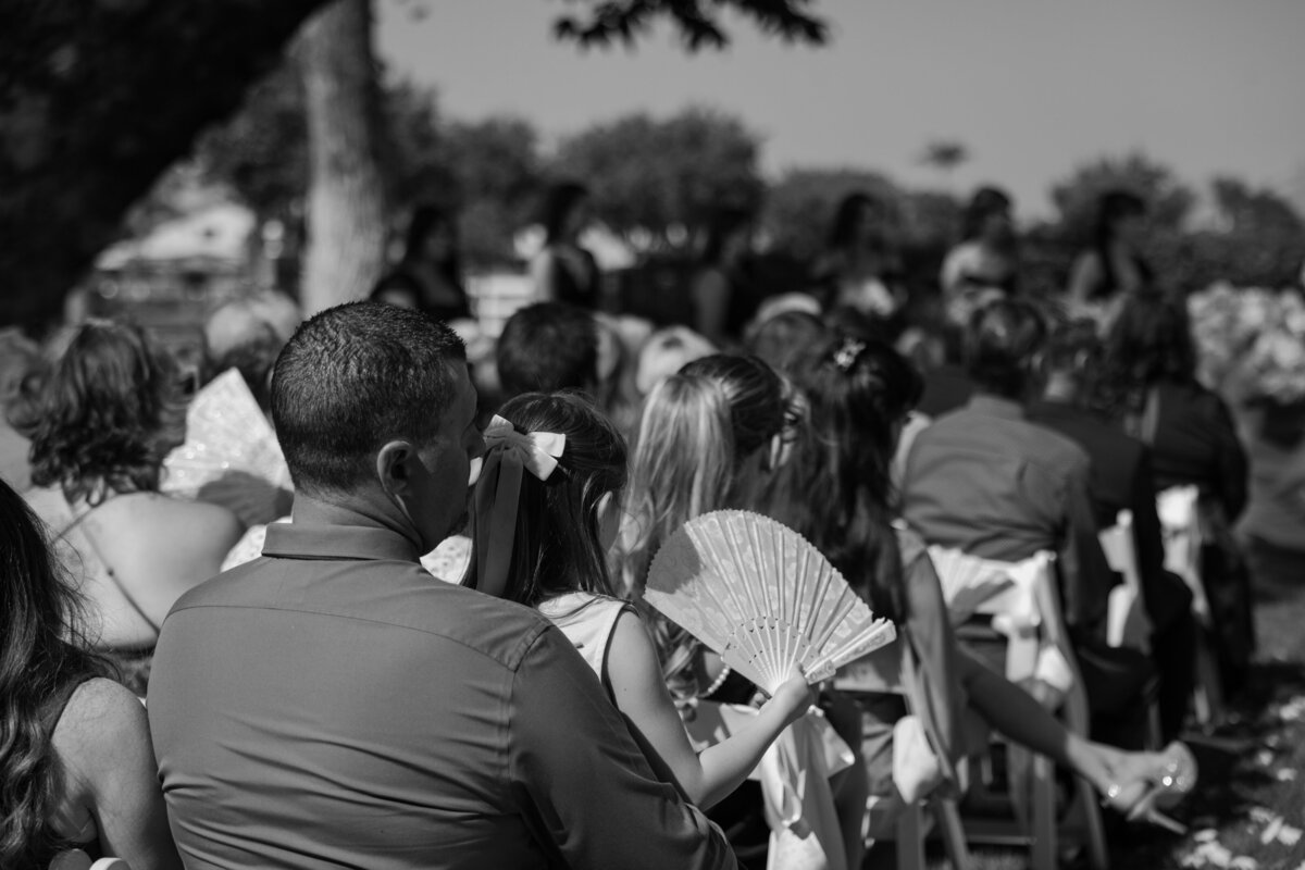 Wedding guests patiently wait for the ceremony to start, in black and white.
