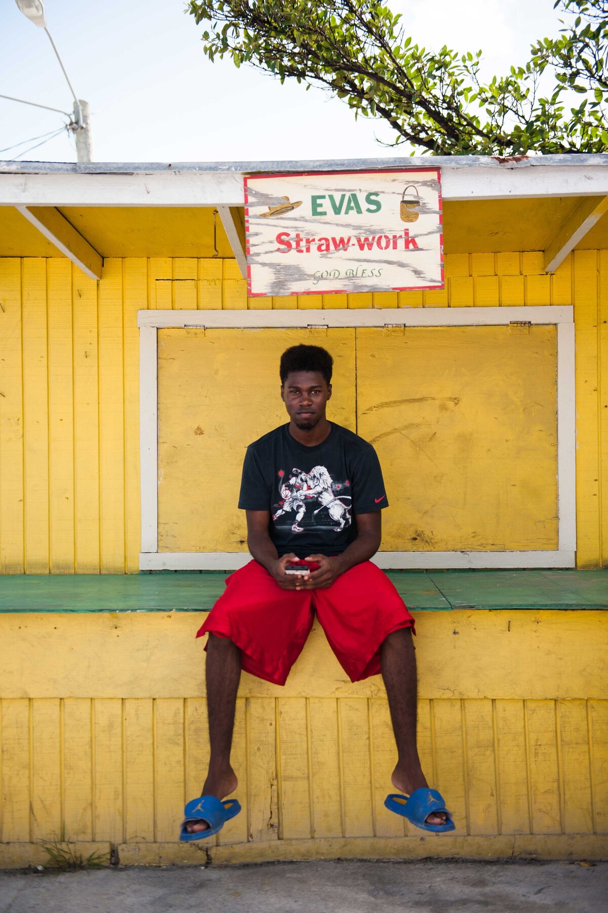 A man in the Bahamas sits in front of Eva's Straw work near Harbour Island port