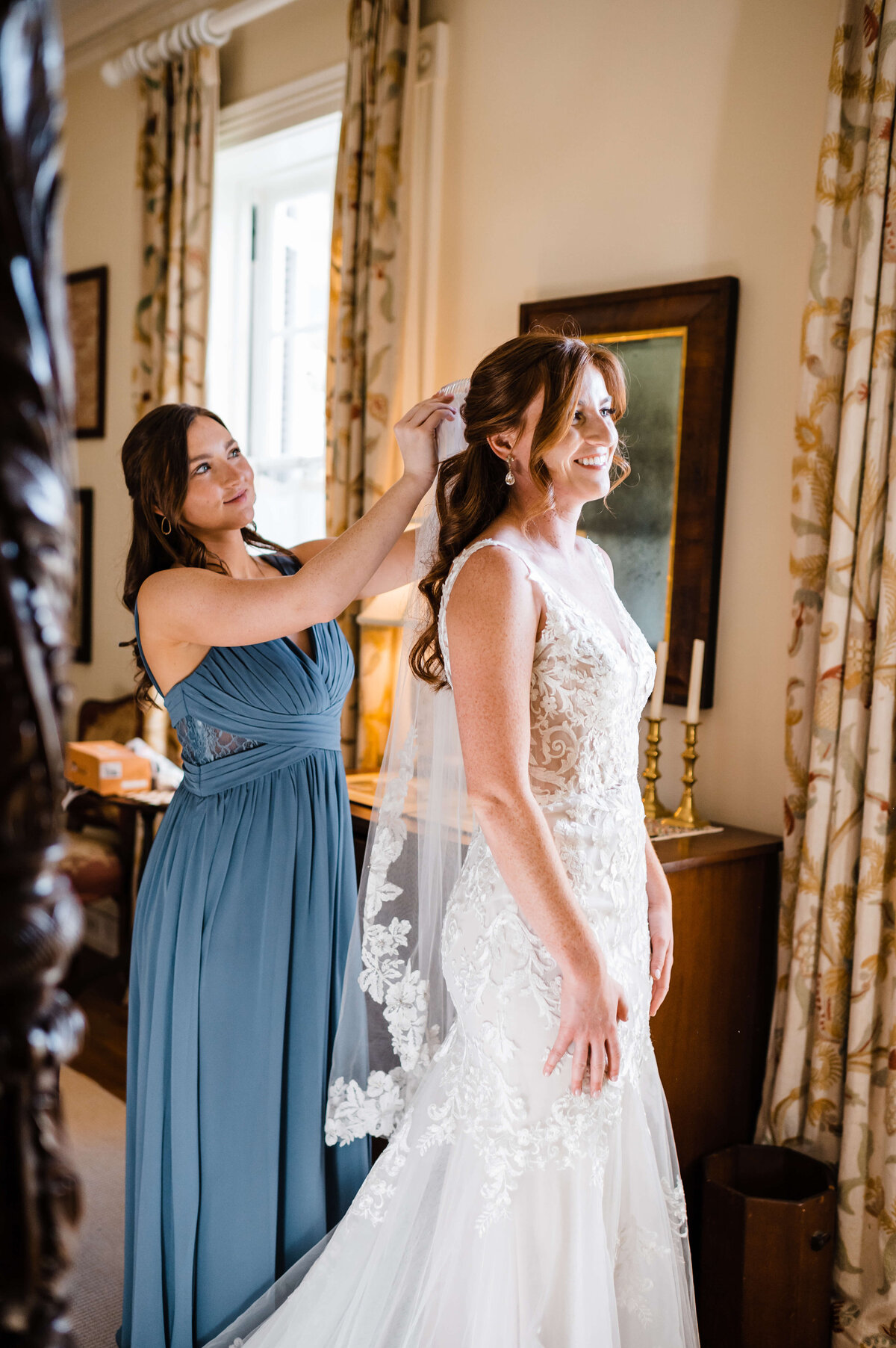 bridesmaid in a blue dress helps the bride put in her wedding veil photographed by Virginia wedding photographer
