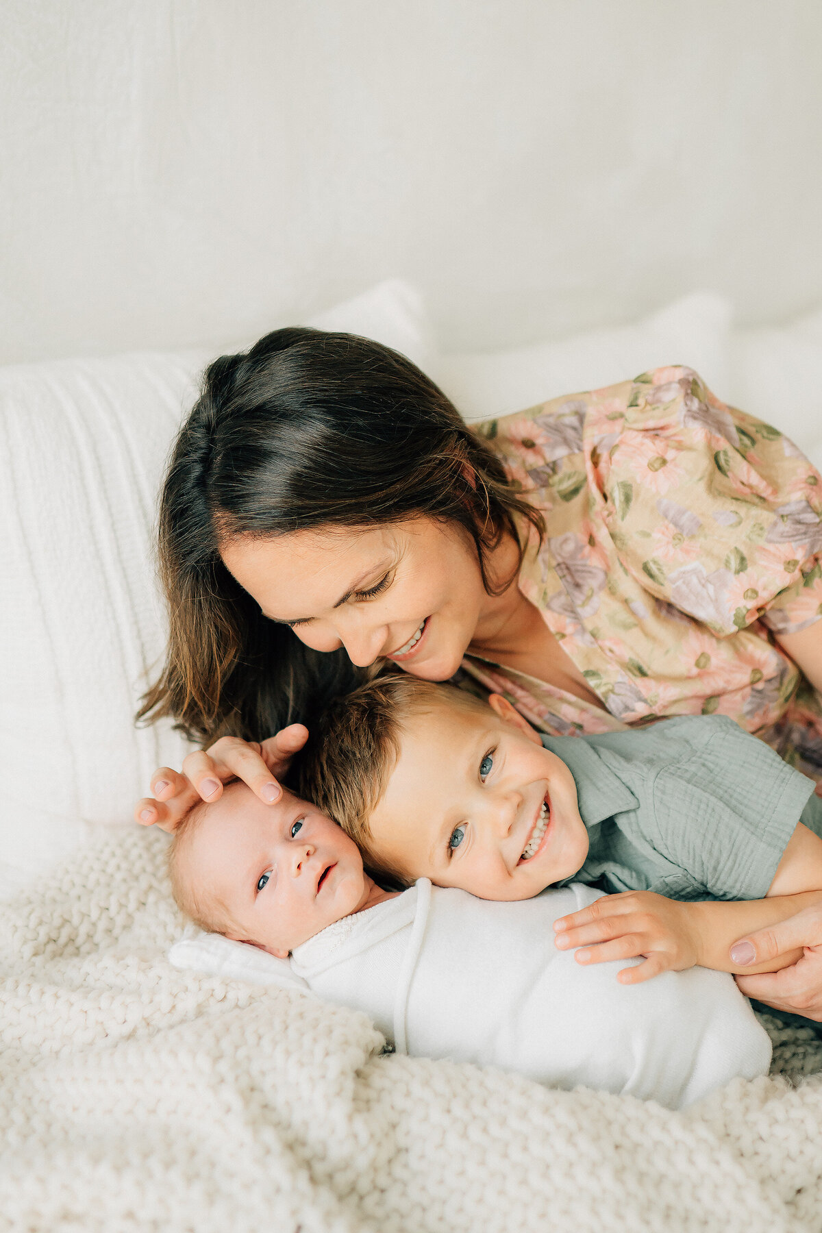 newborn baby swaddled with his toddler brother lying beside him and mom stroking baby's forehead