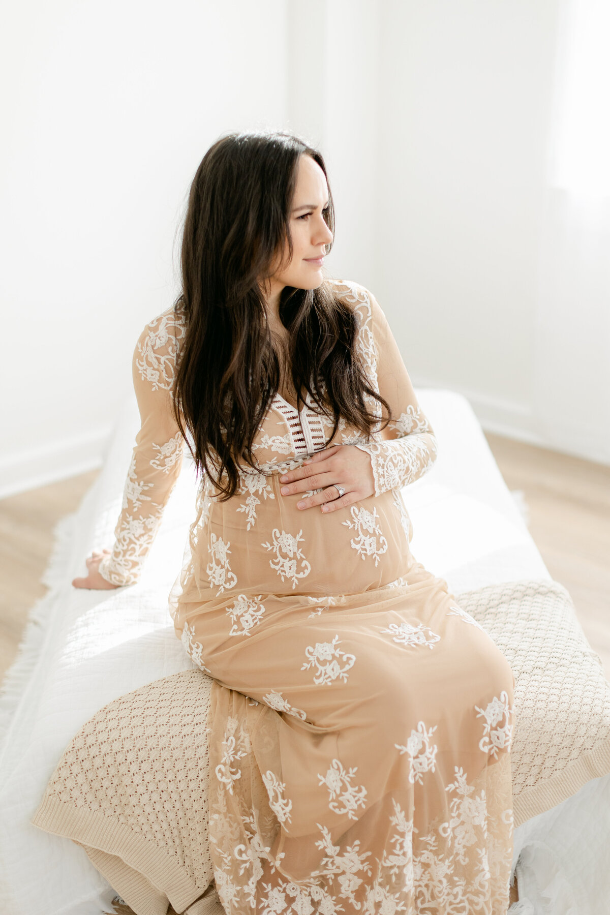 pregnant mom in a lace dress sitting on a bed photographed by Philadelphia Maternity Photographer