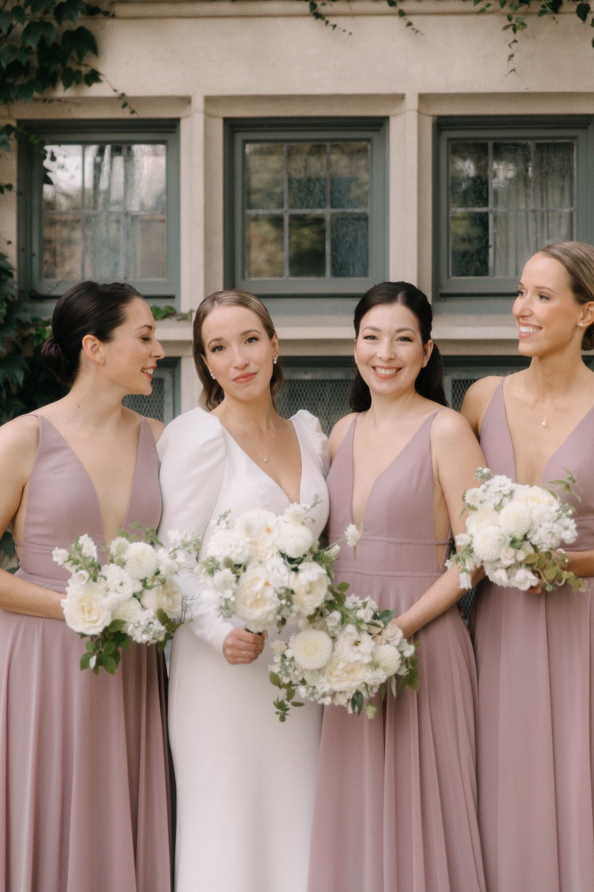 A bride and bridesmaids wearing pale pink dresses hold white bouquets at a Montreal wedding.