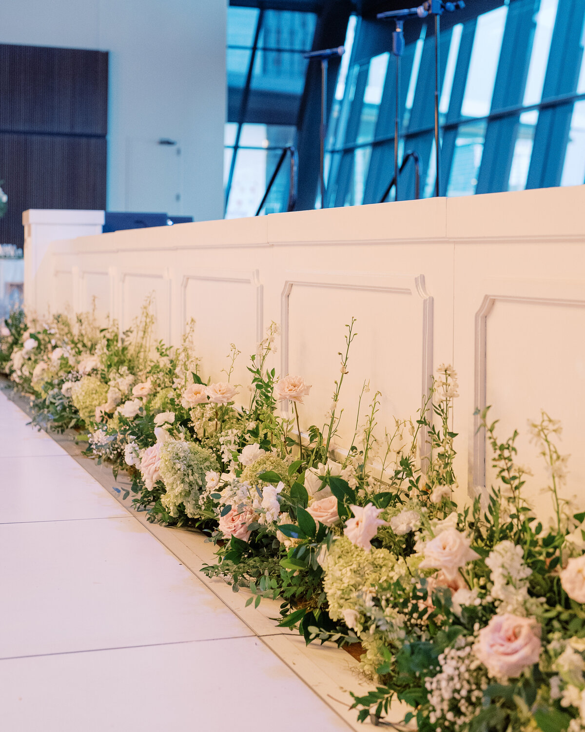 Garden-inspired floral meadows line the front of the stage. Timeless floral design for this garden-inspired floral design. Meadows with roses, baby’s breath, hydrangea, and greenery. Design by Rosemary & Finch Floral Design.