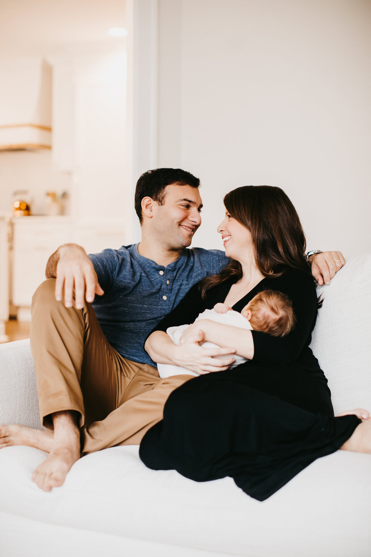 mom and dad holding newborn baby on couch in home