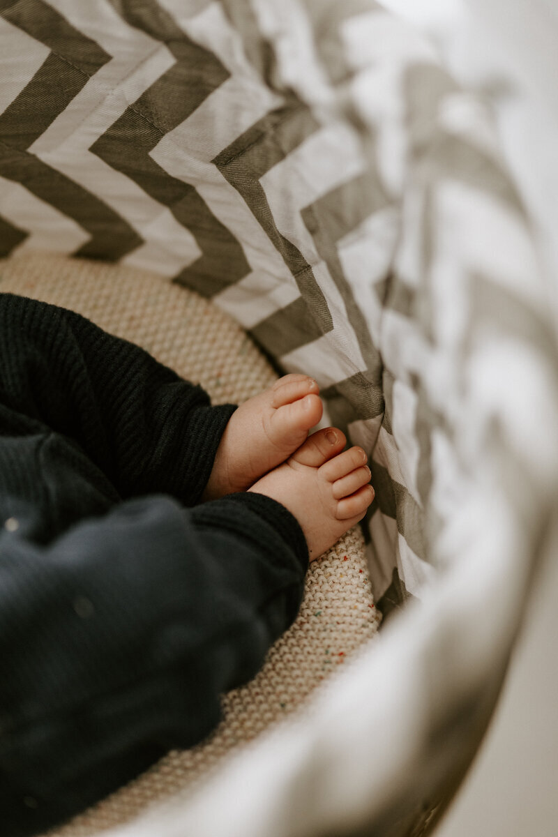 Gros plan sur pieds de bébé dans son panier à rayures pour un shooting photo naissance.