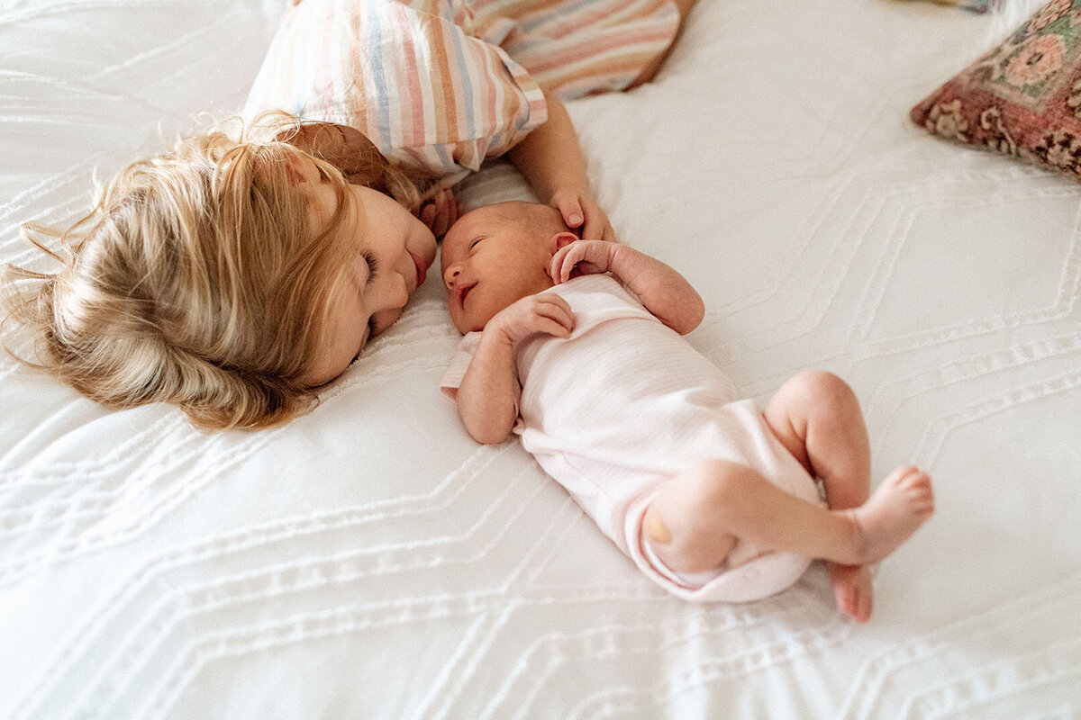 Newborn baby with big sister on bed - Sara James documents sibling bonds and growing family connections during sweet newborn lifestyle sessions in San Antonio Texas family bedrooms