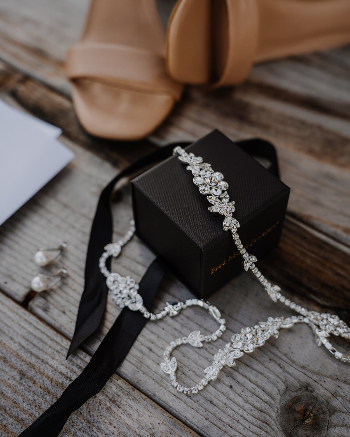 diamond necklace on black ring box next to women's heels