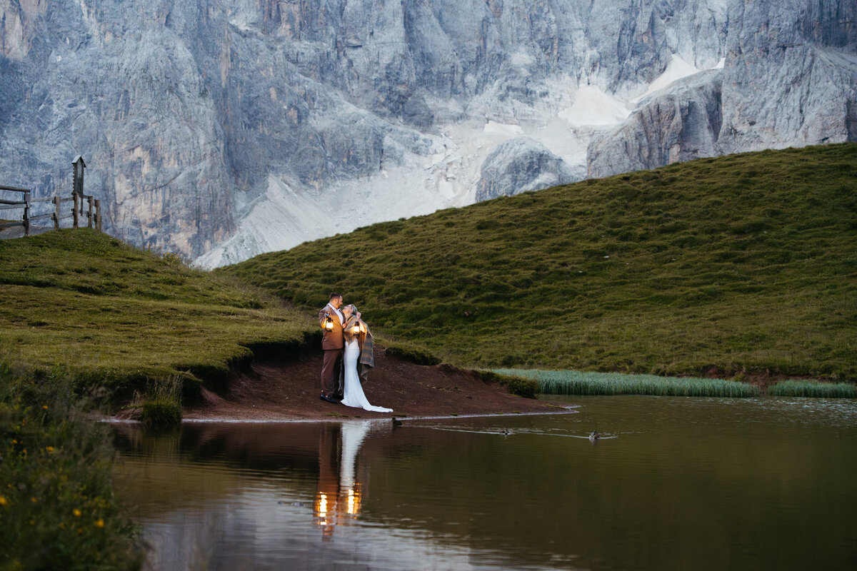 Couple holding lanterns by mountain lake at dusk