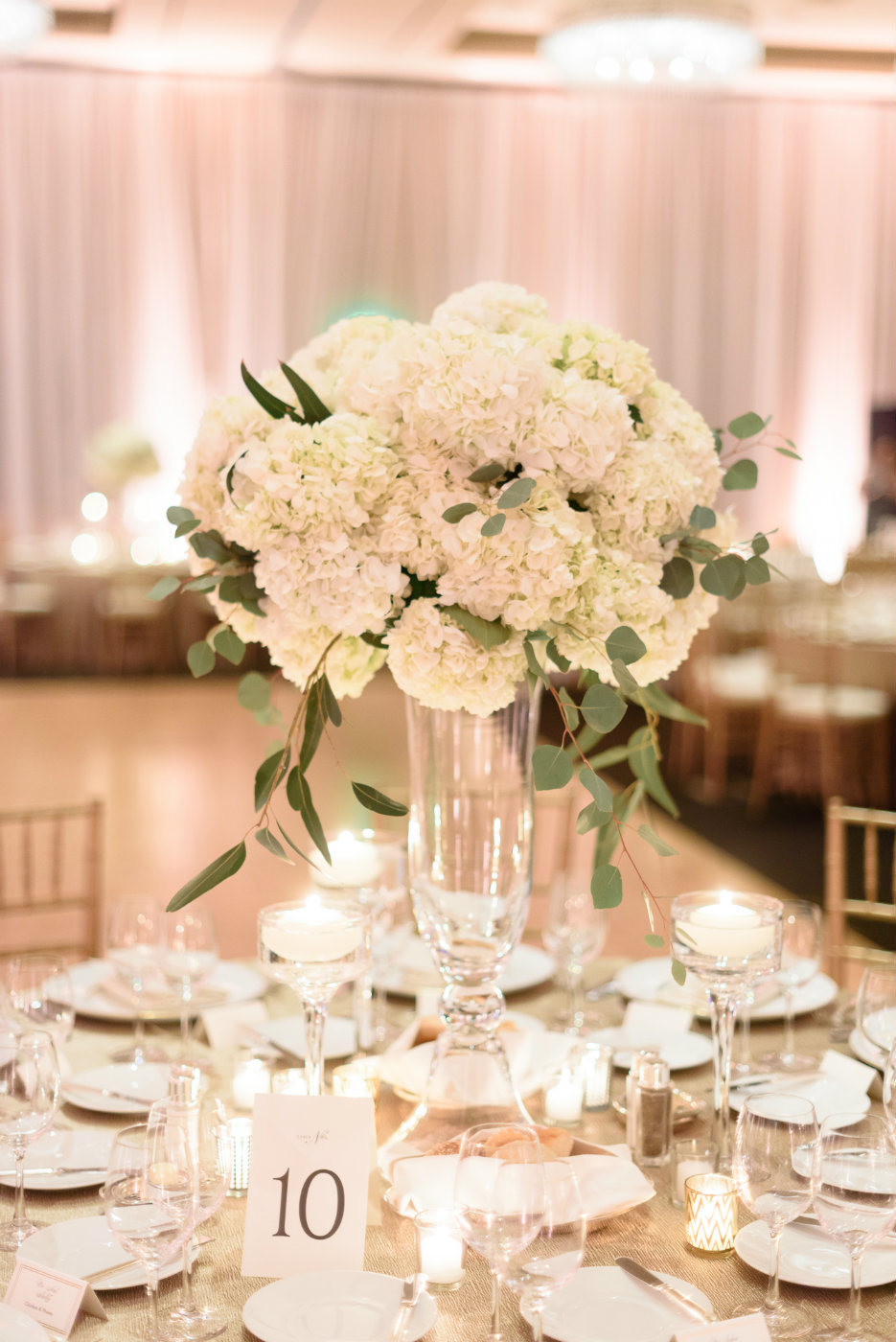 All white hydrangea with eucalyptus atop a tall glass vase is a simple and elegant winter wedding reception centerpiece.