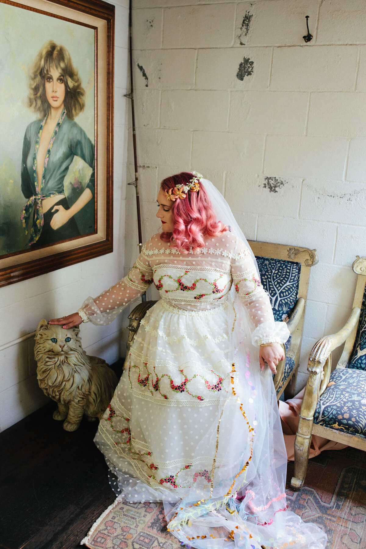 LA rainbow wedding with pink hair bride petting cat with dolly parton painting at smog shoppe
