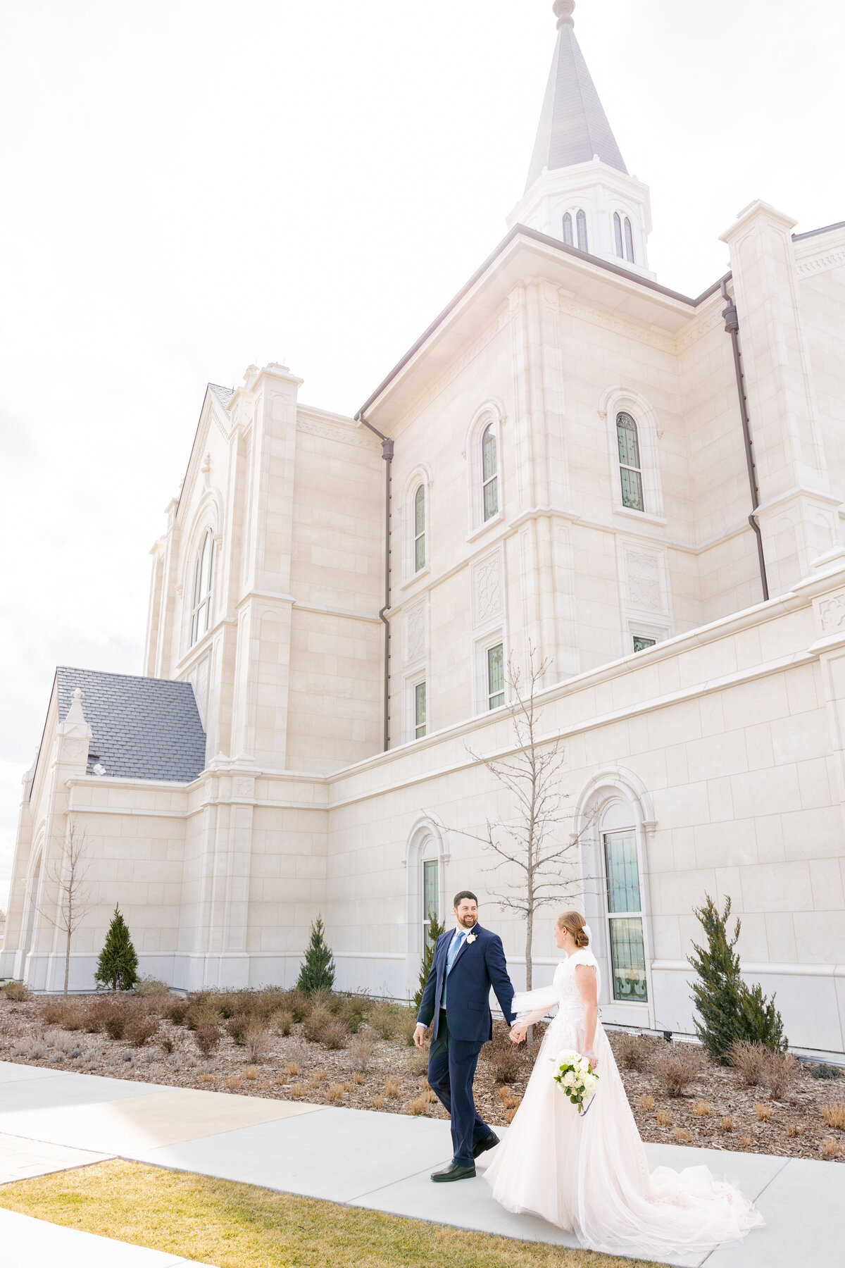 Bride and groom holding hands and walking joyfully outside the Taylorsville Utah Temple after their ceremony.