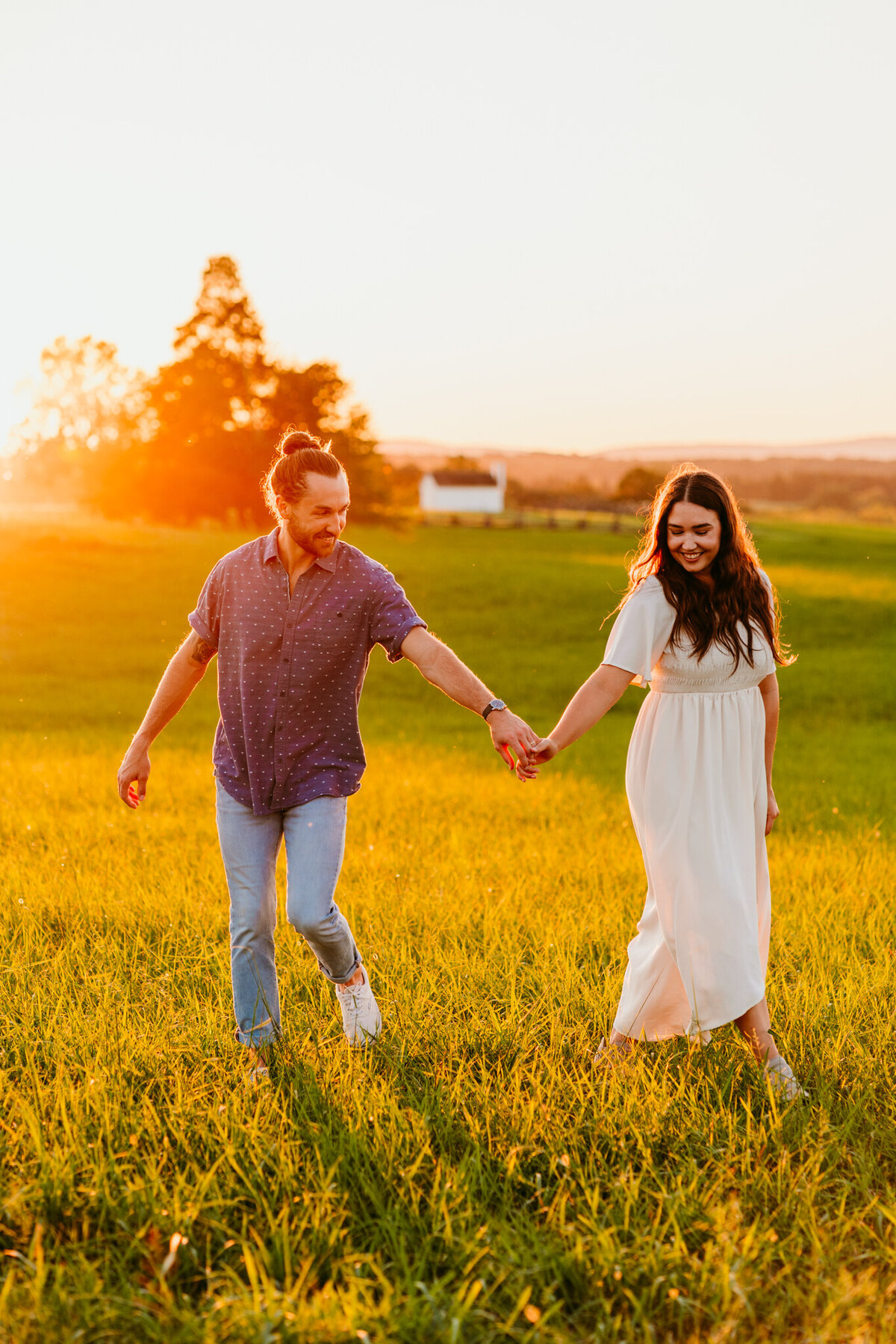 Couple holding hands and walking through golden sunset field