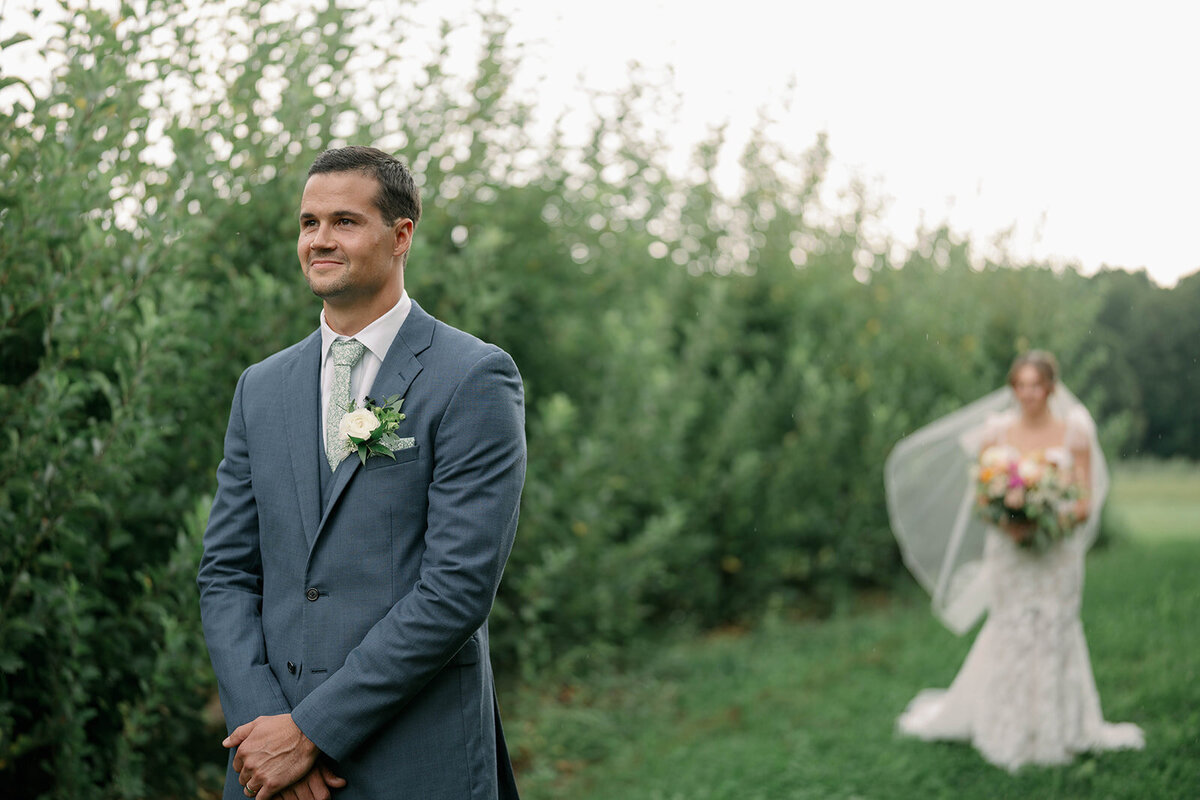 Bride walking up behind the groom for their first look moment before the big reveal at their September Cherry Barn wedding in Frankfort MI.