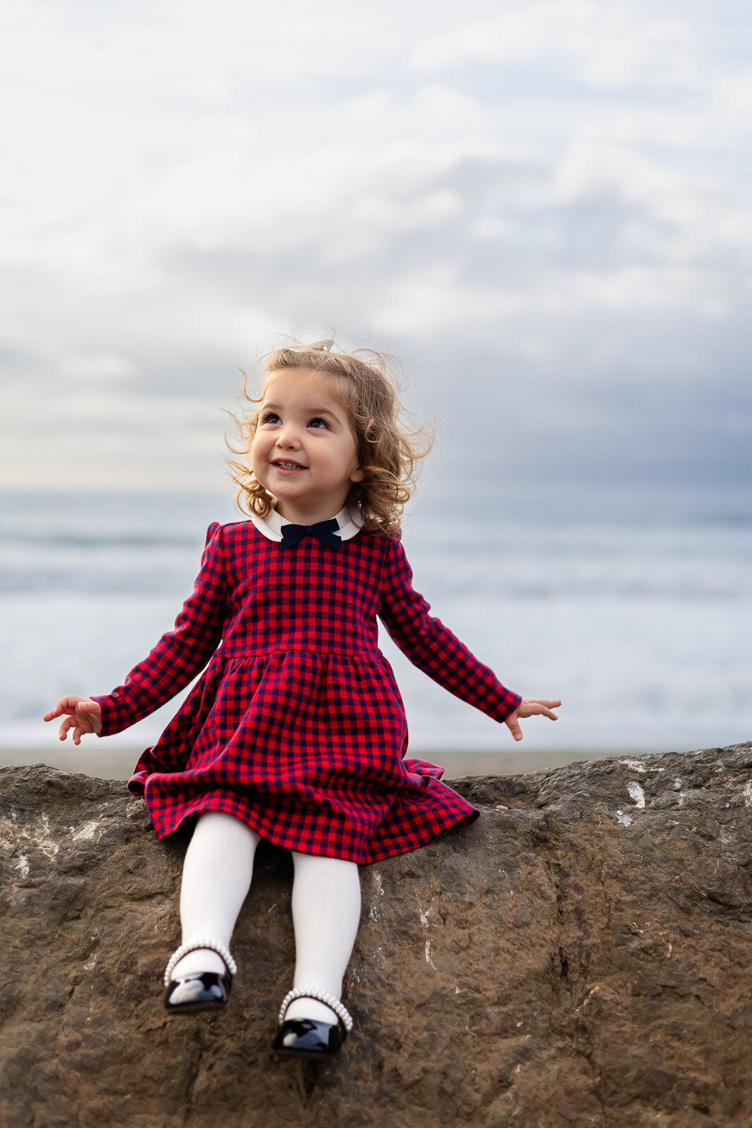Toddler in red plaid dress smiling near the ocean in Pacifica – Bay Area Family Portfolio – Ellobelle Photography