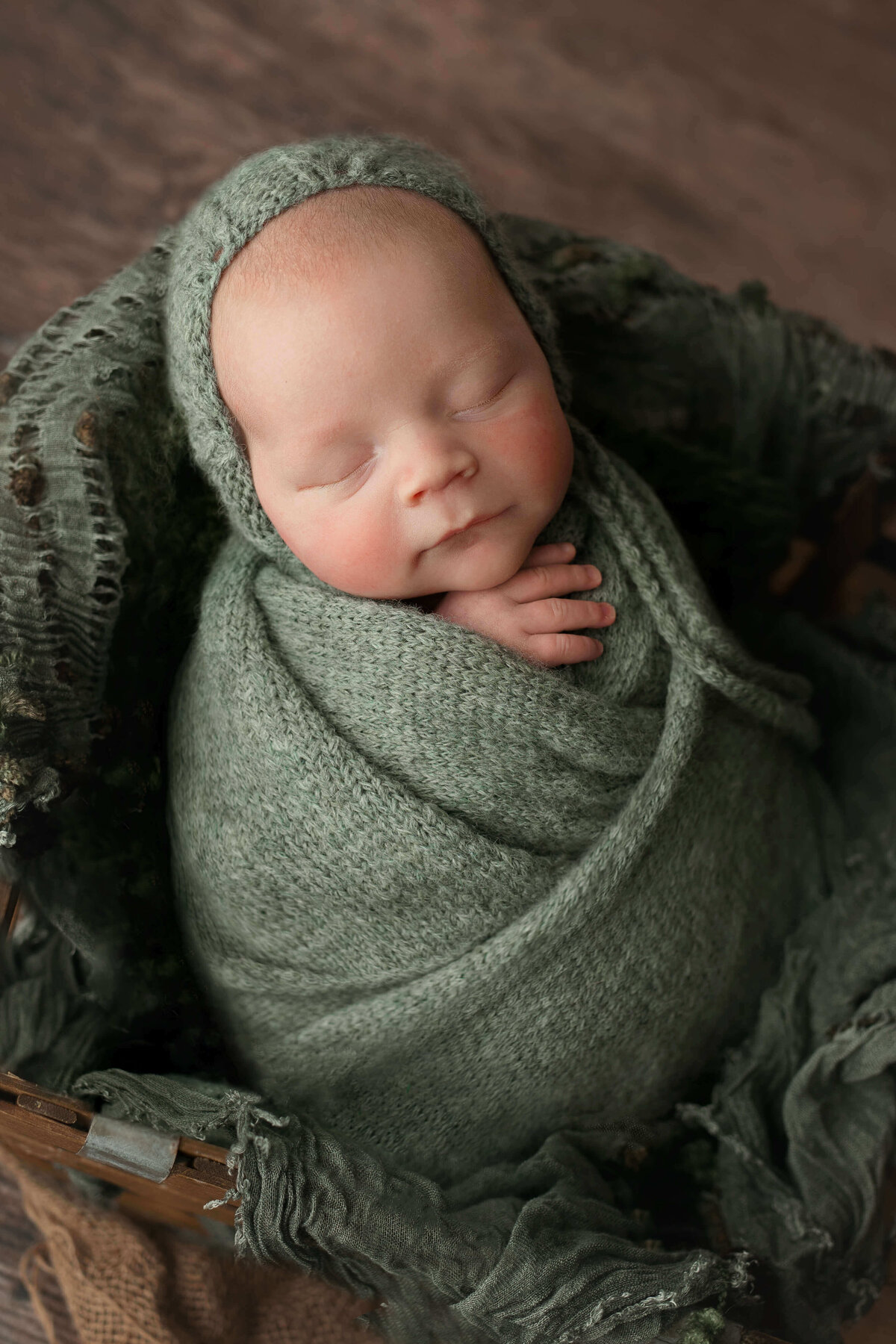 newborn boy in a green wrap and bonnet  at his newborn photo session
