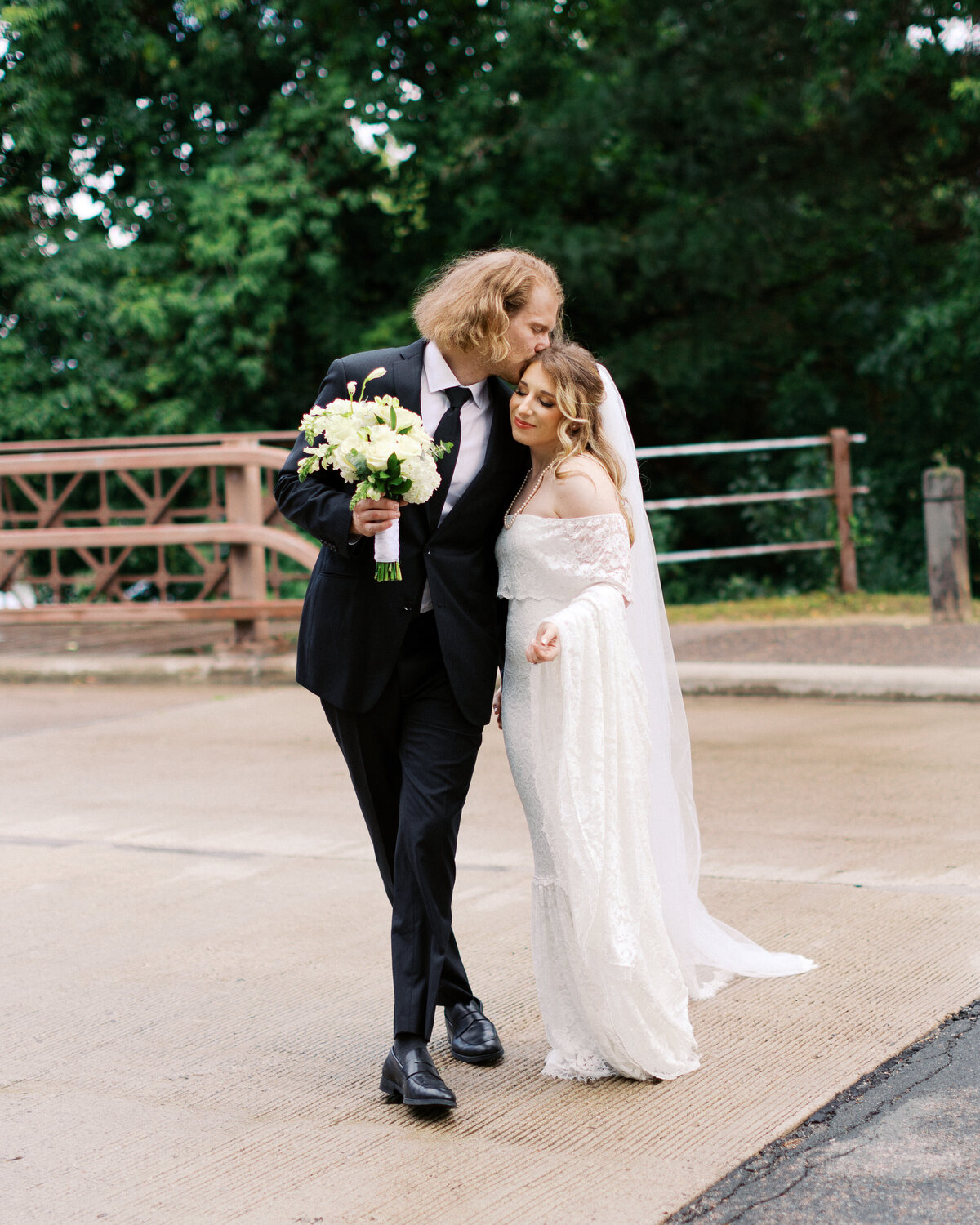 Newlyweds crossing the street in minneapolis while he gently kisses her head in the romantic moment at their Nicollet Island Inn Wedding.