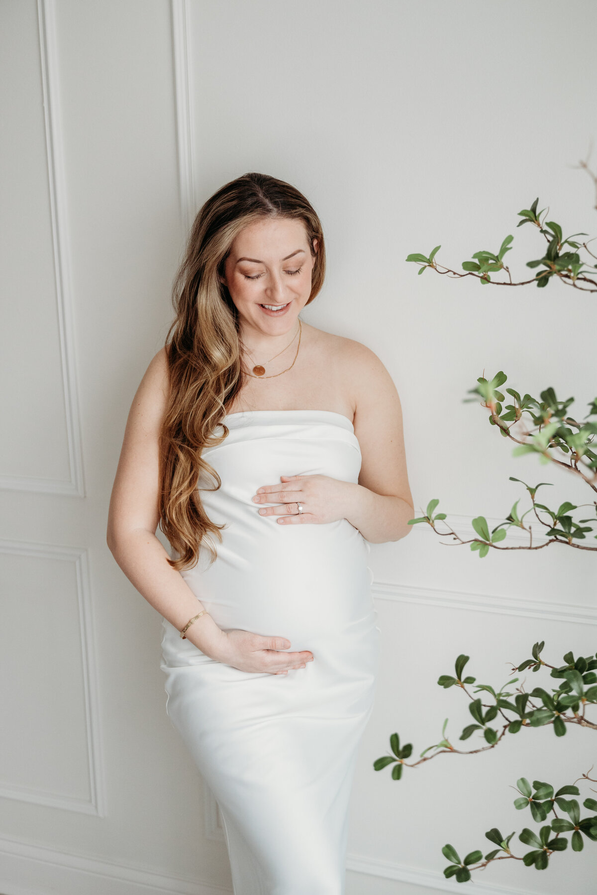 Beautiful, glowing mom to be feeling her baby kicks while leaning against a wall in a brigh studio in Bartlett, IL