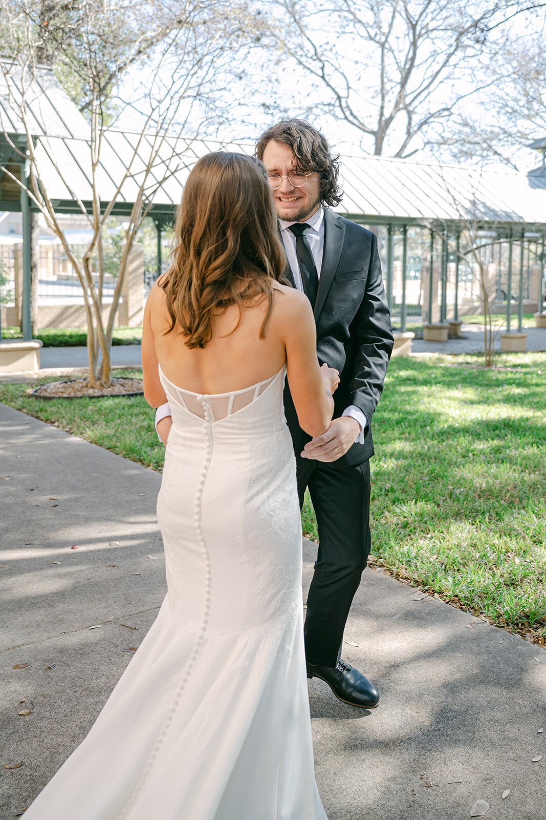 Editorial image of couple turning to see each other during first look through sunlit path at San Antonio wedding location