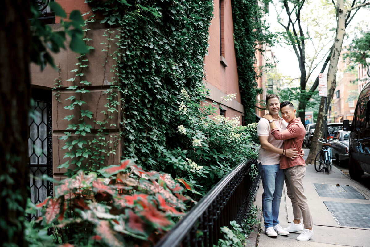 The engaged couple is hugging each other sideways, beside an ivy-covered building at West Village, NYC. Image by Jenny Fu Studio.