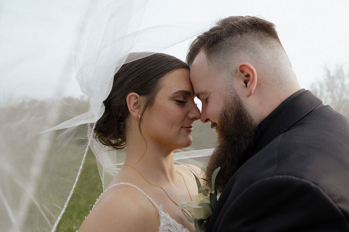 Bride and groom touching foreheads, veil flowing