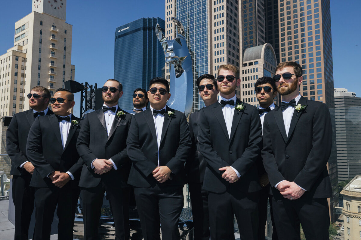 Groom and groomsmen in black suits and sunglasses looking stylish on The Statler rooftop near the llama sculpture