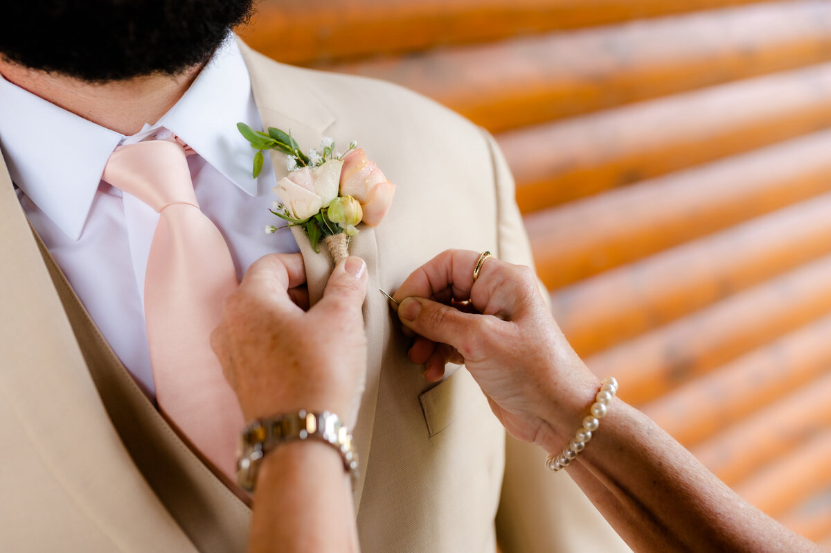 mother of the groom puts on his boutonniere to his tan suit with a pink tie