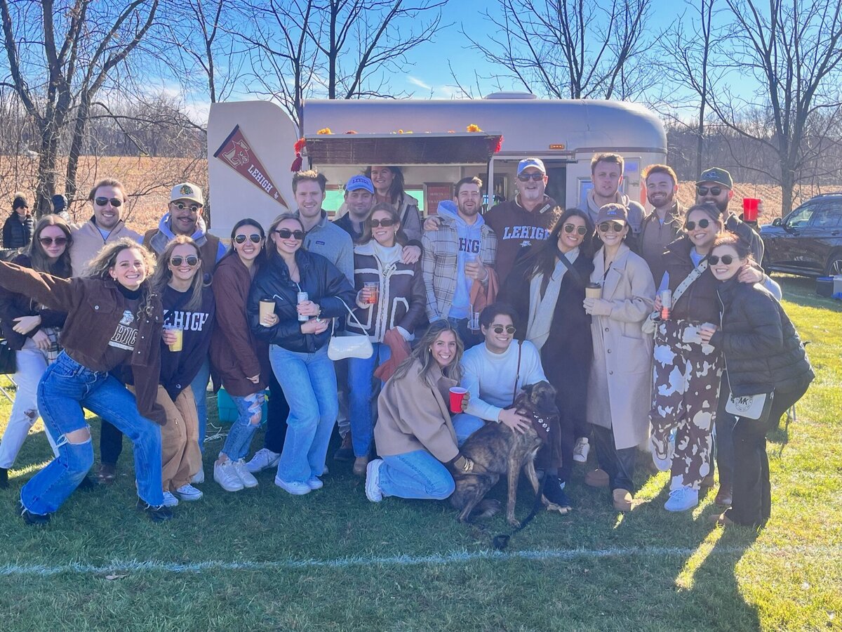 Group of college alumni stand outside Sol & Spirits trailer at tailgate event