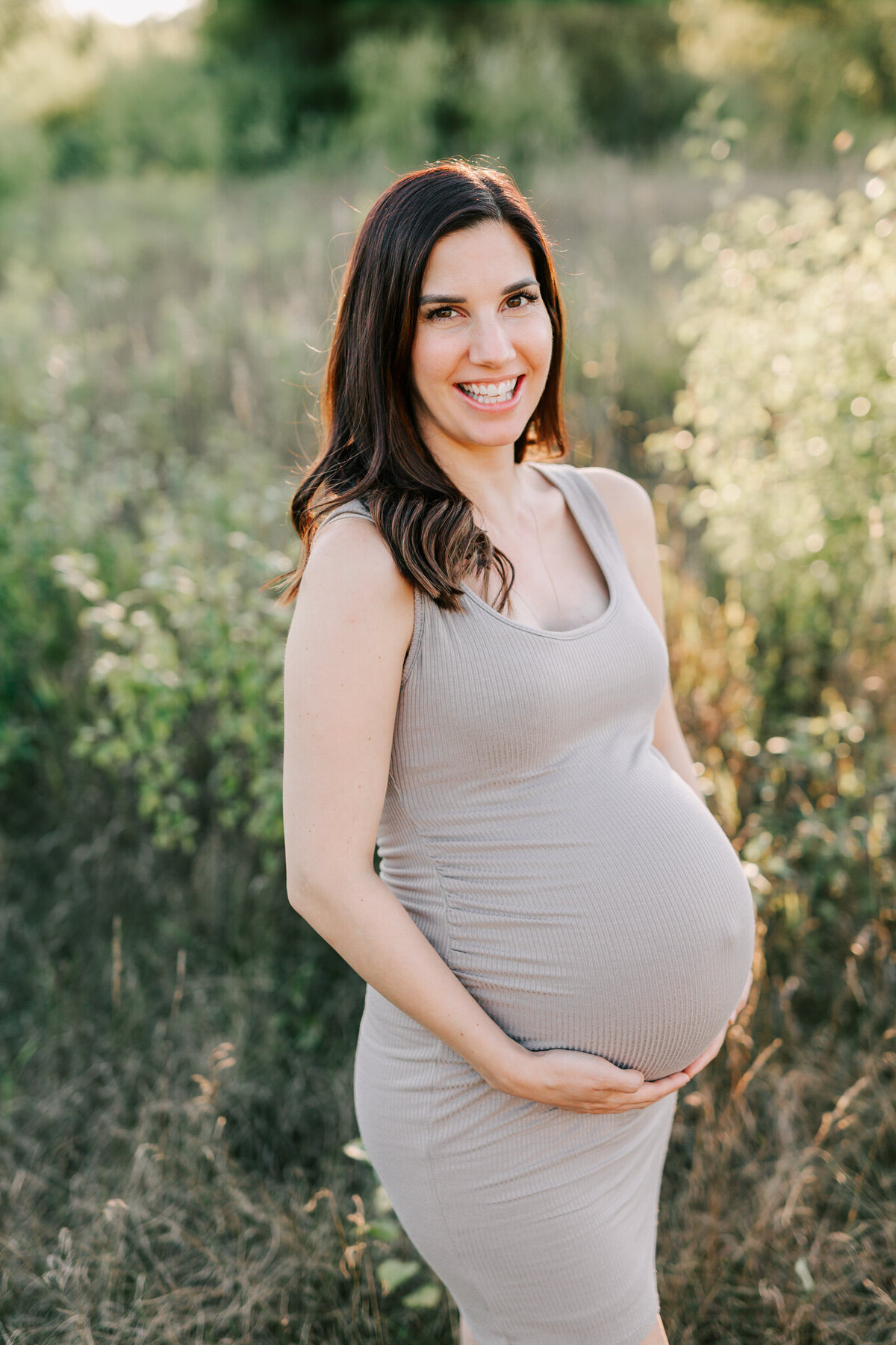 Expecting mother grins in the field during her maternity session with Chelsey Kae Photography