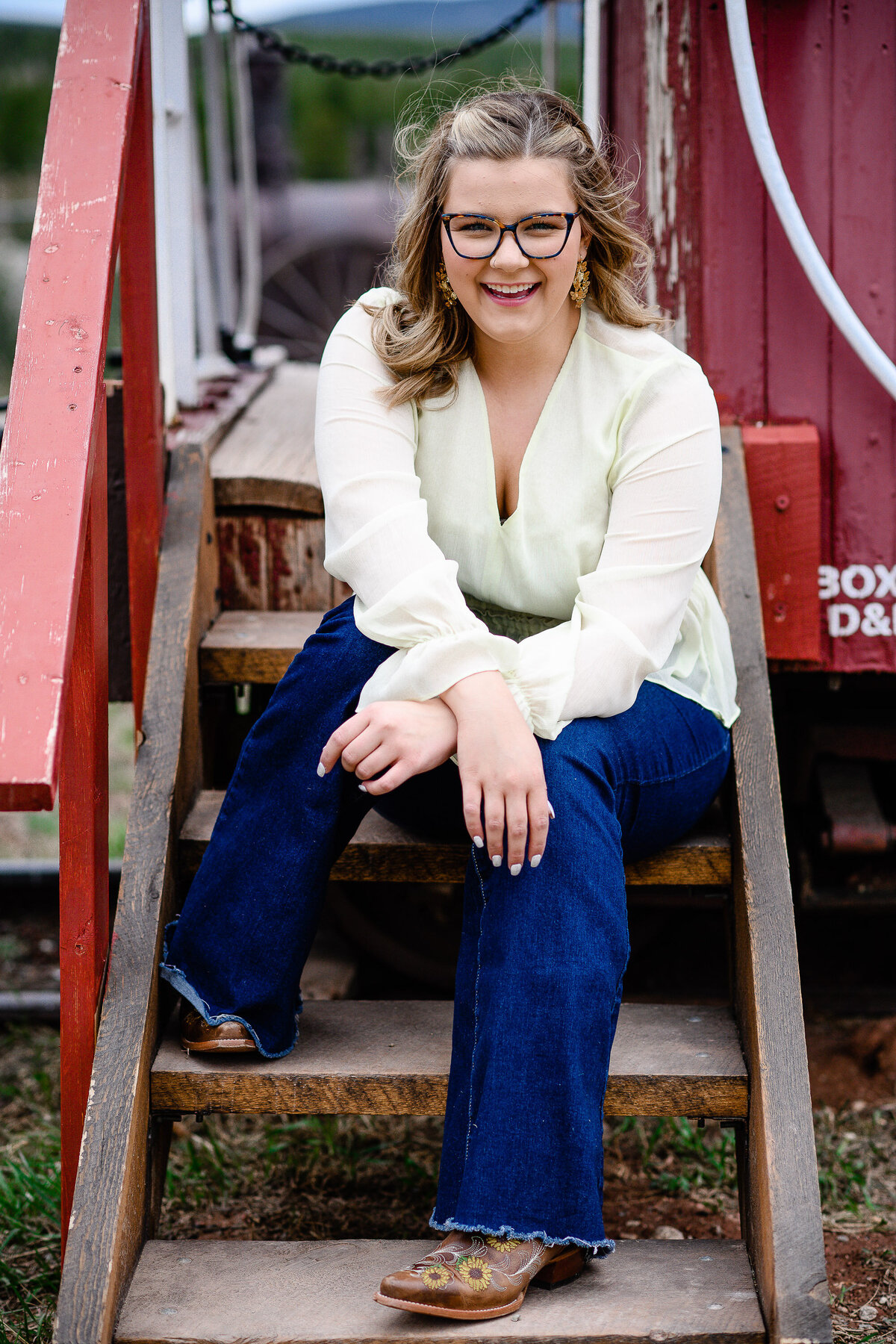 high school senior sitting on stairs of a train while wearing a cream blouse and jeans for her senior photo outfits ideas captured by denver senior photographer