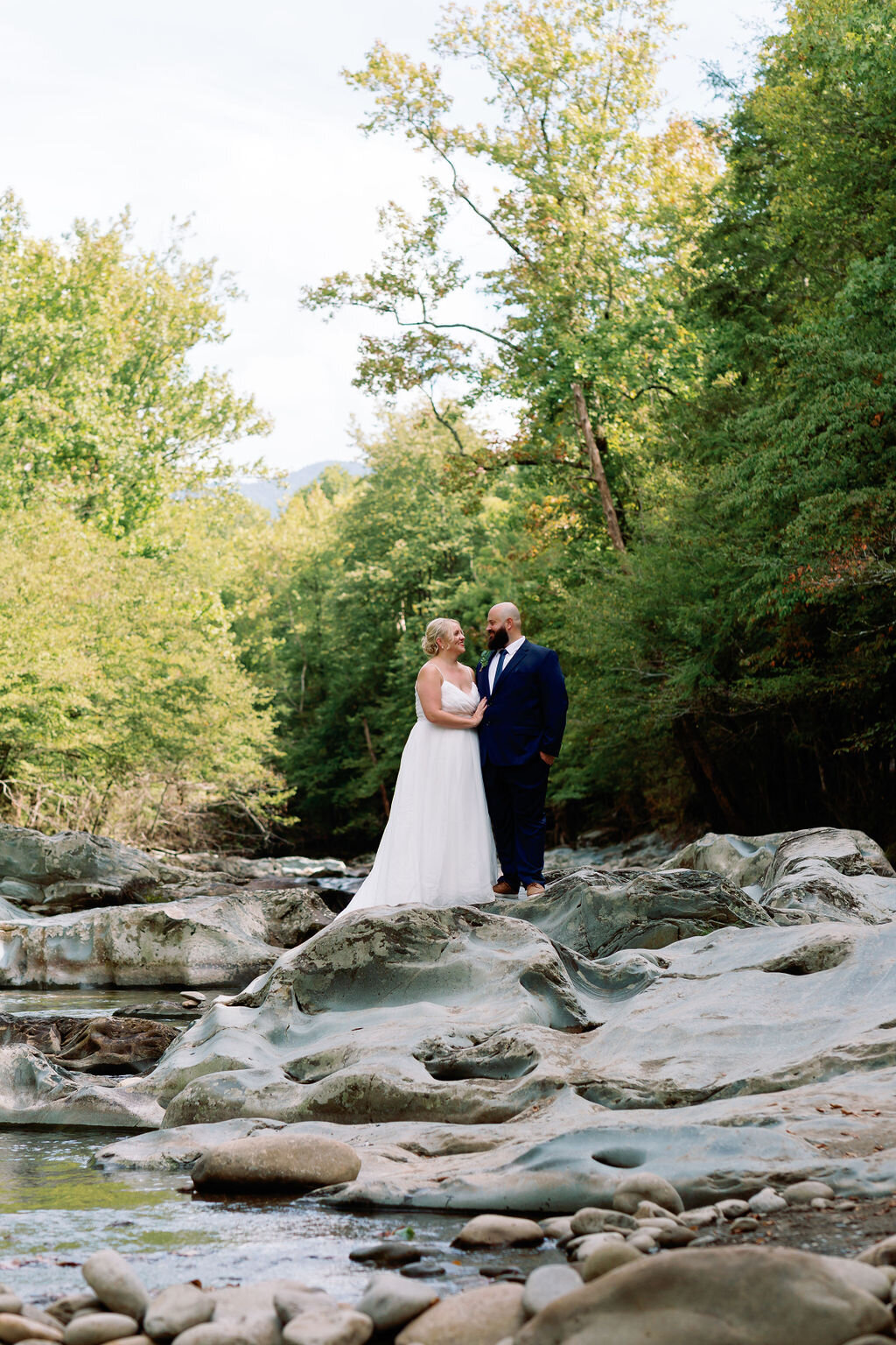 Bride and groom standing together on weathered rocks in the Greenbrier area, gazing at each other with forested mountains behind them during their eloping to Gatlinburg celebration.
