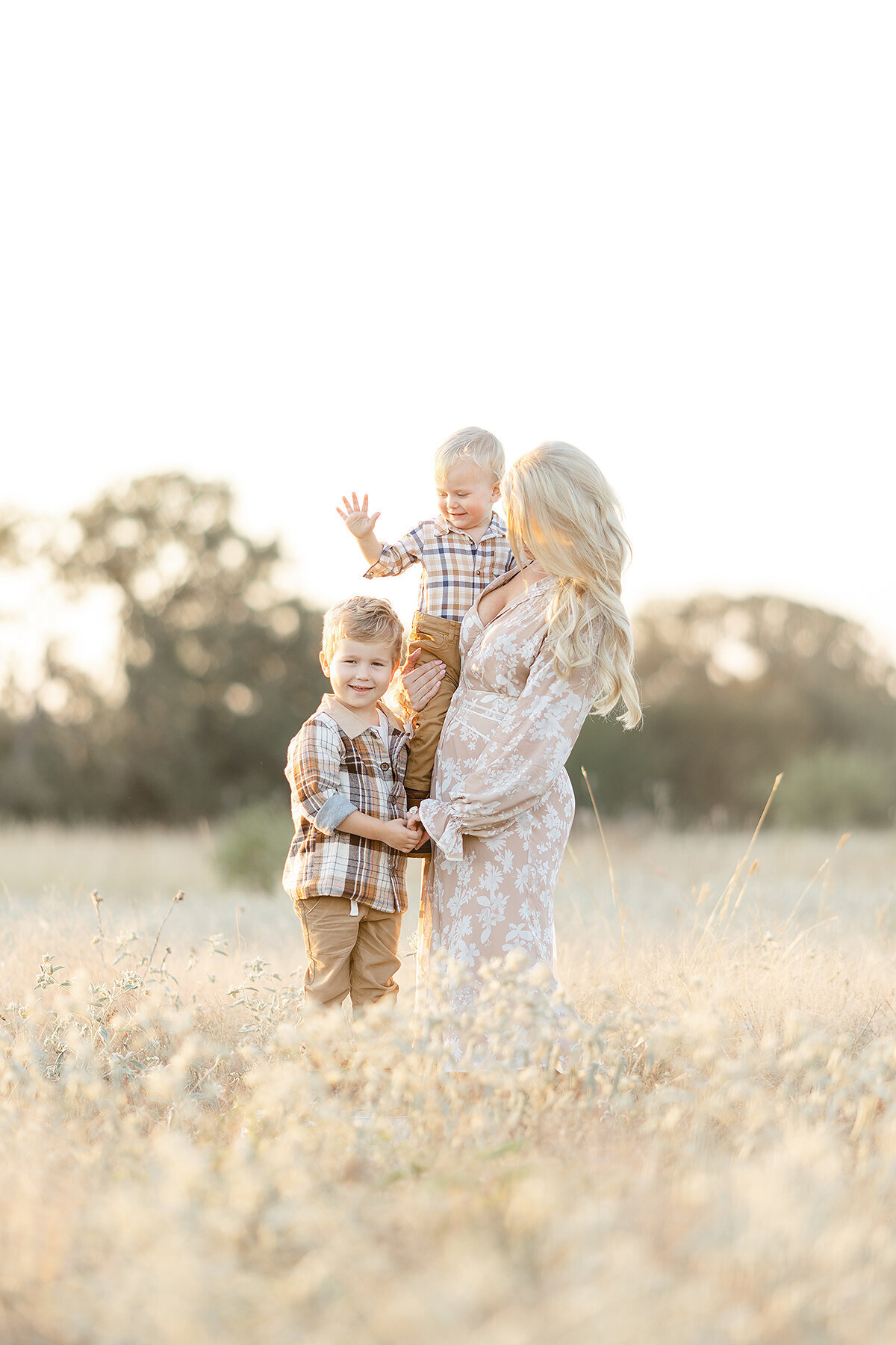 A mother standing on the middle of a field with her 2 sons.