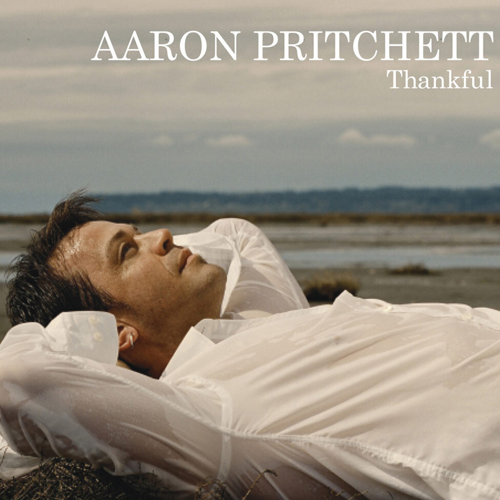 Album CoverTitled Thankful Artist Aaron Pritchett lying on his back on beach arms folded behind his neck looking up at sky wearing wet white dress shirt