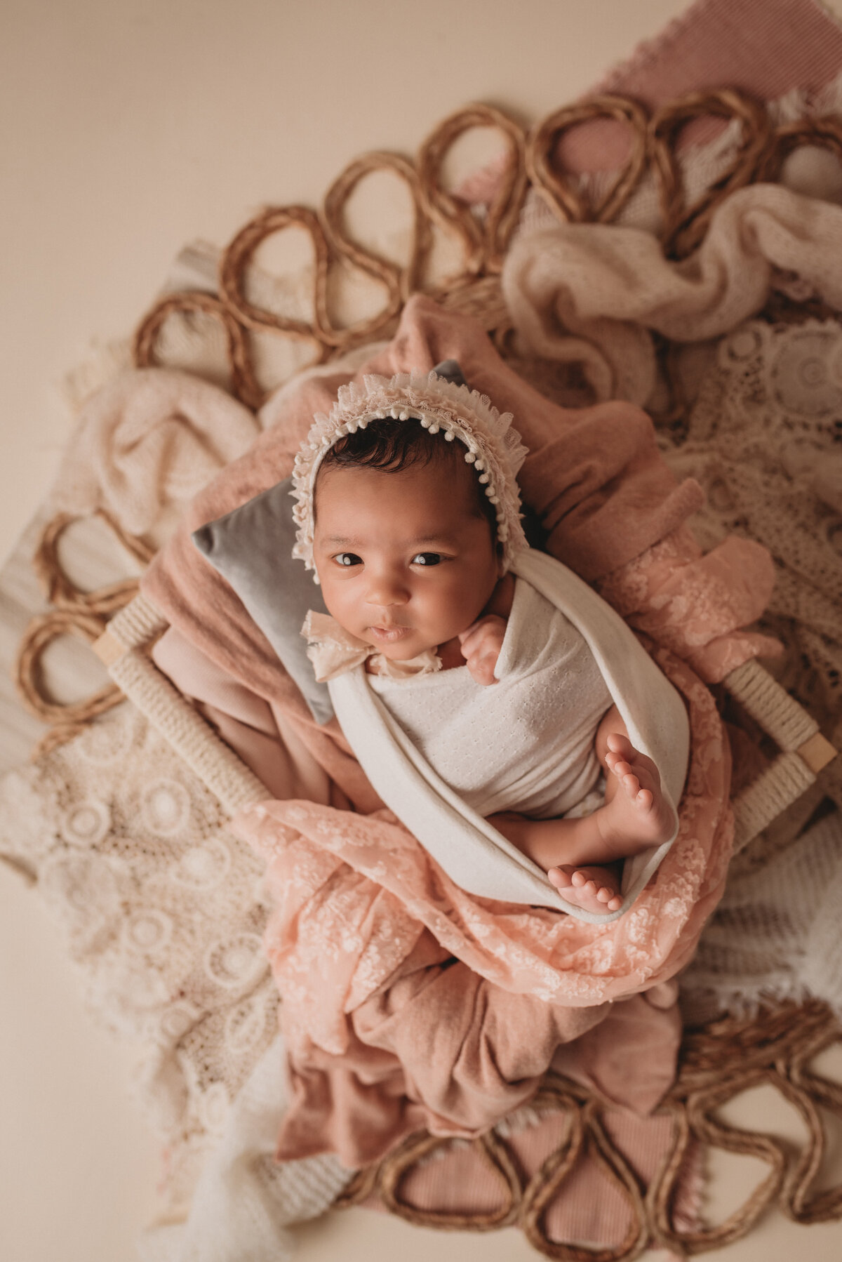 Baby girl at her newborn portrait session in  pink and white hat laying in boho themed creams and tan setup