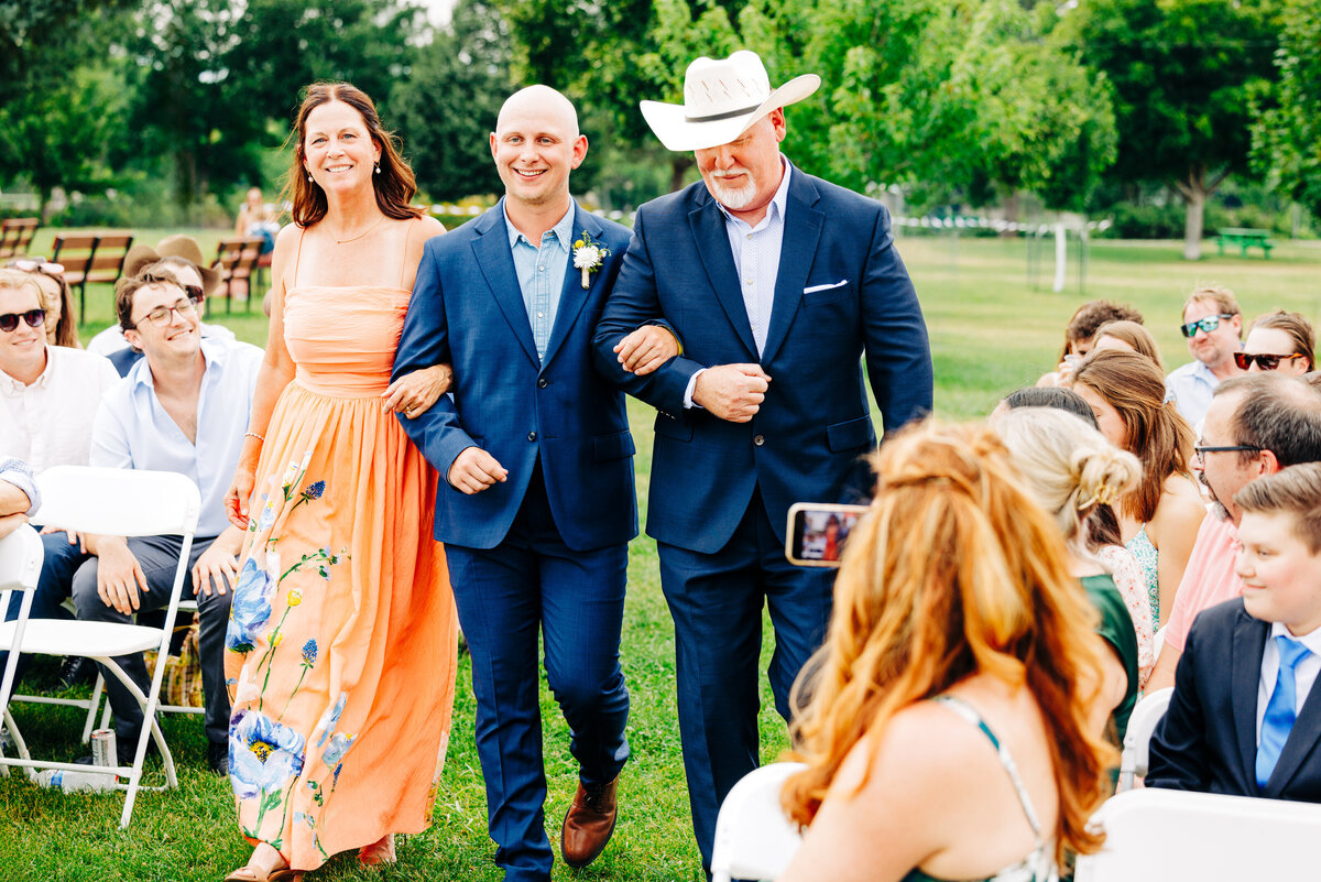 Groom being escorted down aisle with parents at Miles Park Band Shell in Livingston, MT