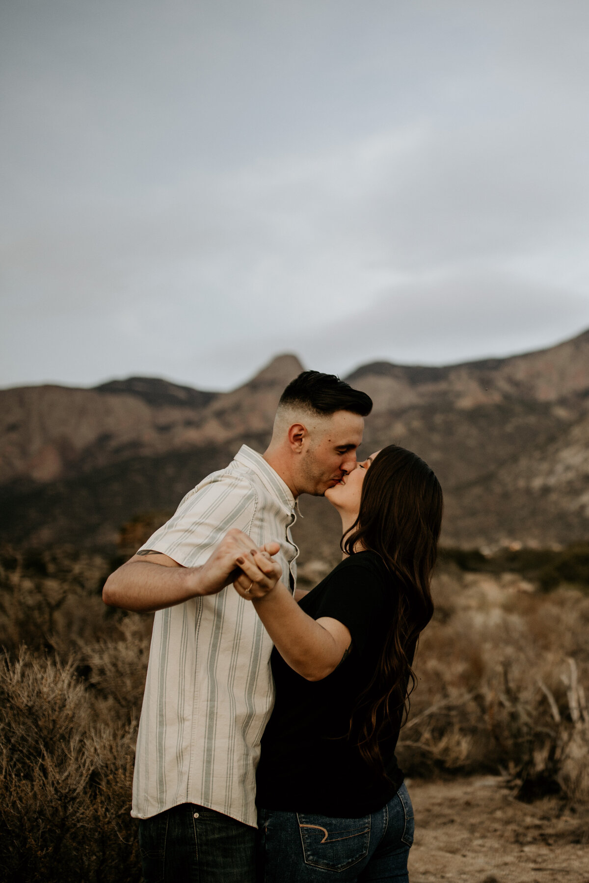 engaged couple holding hands and kissing in front of a mountain