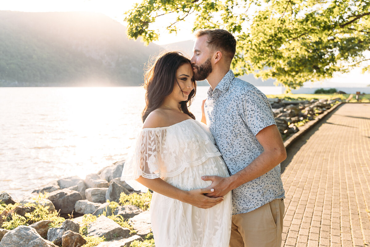 Maternity Photographer, a man kisses his pregnant wife on the forehead near the lake