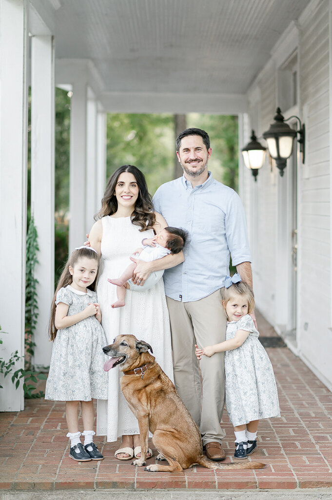 Family stands on a porch with their 3 children and dog