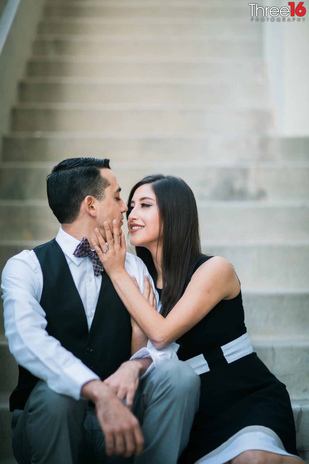 Bride to be places her hand on her Groom's face as they sit together on the stairs