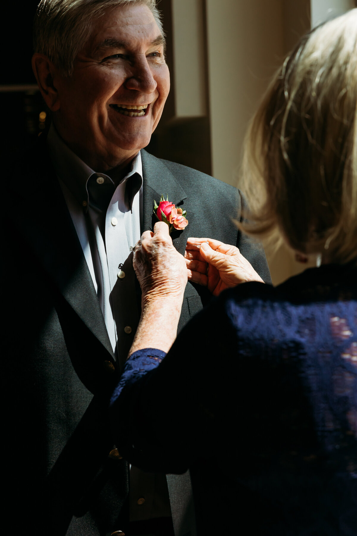  A sweet candid moment as a woman pins a boutonniere on a smiling guest, captured during a joyful Florida wedding morning.