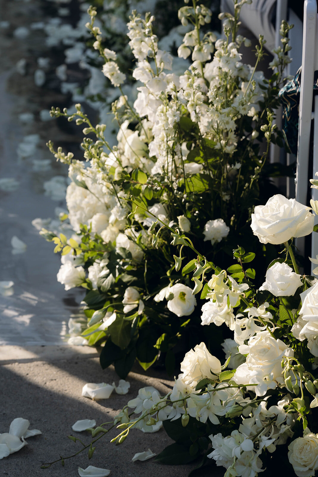 A lush white floral arrangement at a luxury wedding ceremony, with delicate petals scattered along the aisle. A refined and elegant detail shot capturing the beauty of high-end wedding decor.