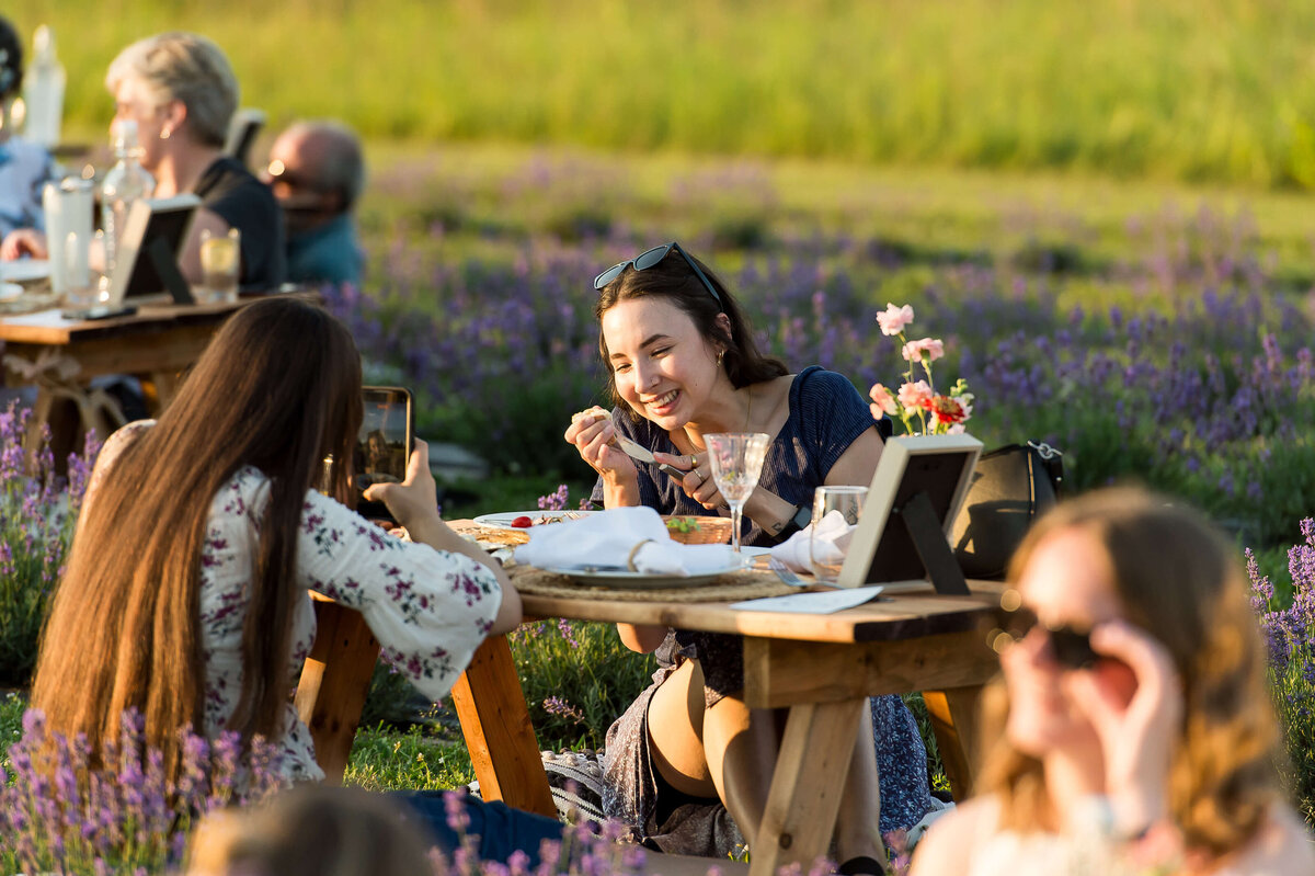 women laughing and sitting at a picnic charcuterie as part of Soiree in the Field.  Captured by Ottawa Event Photographer JEMMAN Photography COMMERCIAL
