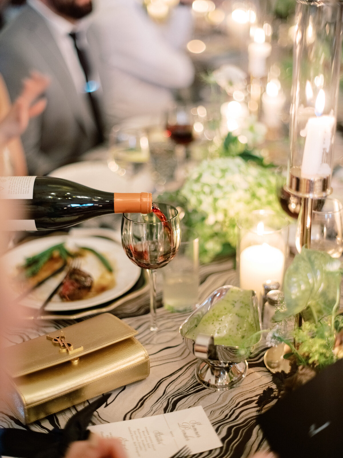 A hand meticulously pours red wine into a glass, set amidst an elegant dining setup, showcasing the beauty of fine dining and celebratory moments filled with taste and elegance.