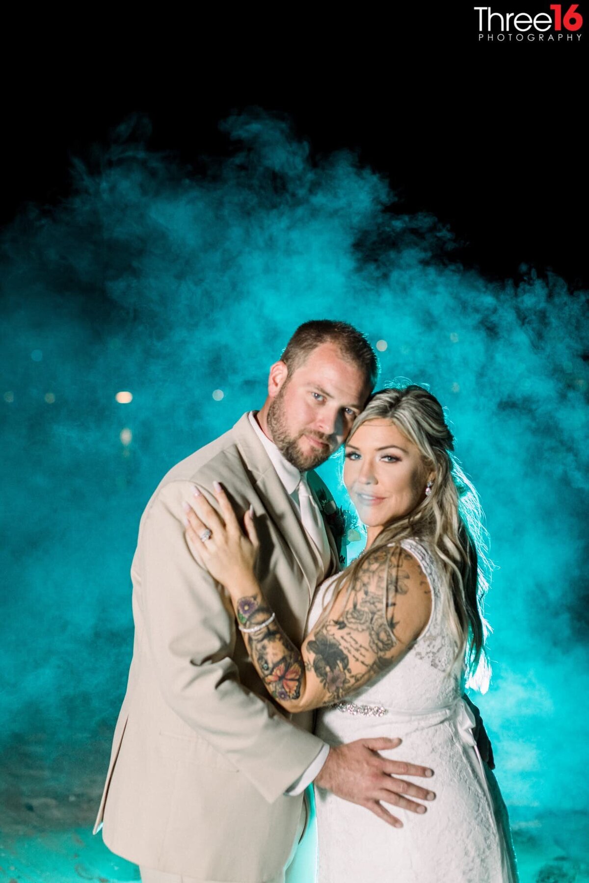 Bride and Groom cozy up to each other as they pose for photos in front of a blue mist