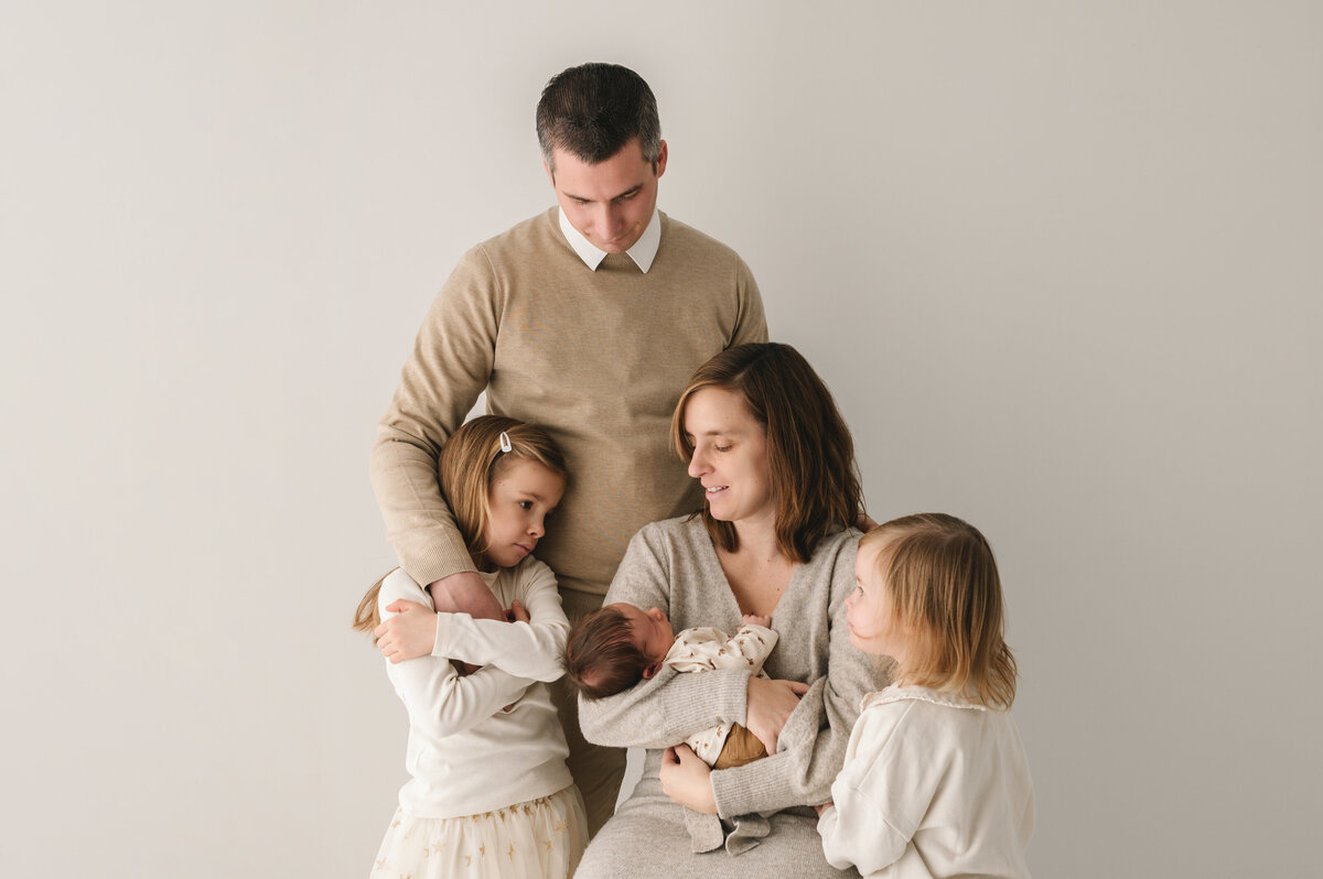 liefdevolle gezinsfoto met pasgeboren baby en 2 grotere zusjes in neutrale setting
