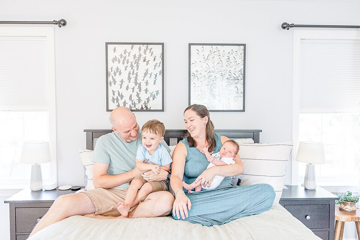 family laughts on bed dung in-home newborn photo session with Sara Sniderman Photography in metro west Boston  Massachusetts